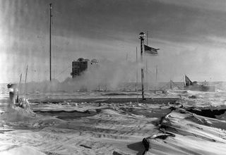 In 1957, the iconic striped pole marking the South Pole flies the American flag. The pole itself stood atop the station. Inside, a team of more than a dozen scientists, mechanics and other staff were the first humans to spend an austral winter at the bottom of the world. The United States has had people stationed the Pole year-round ever since.