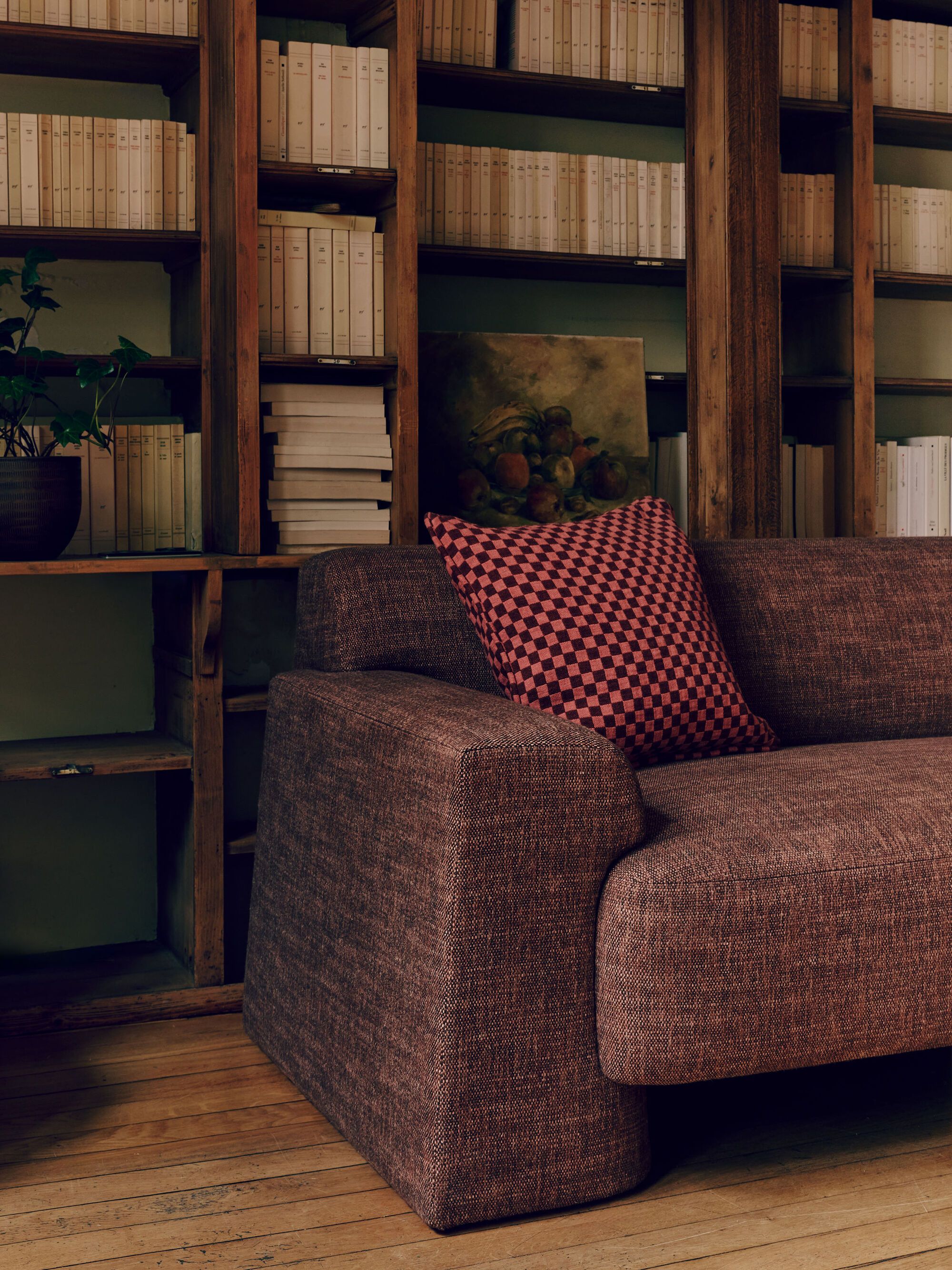 Image of a purple and pink sofa with a purple and pink checkerboard pillow in front of a vintage wooden bookcase.