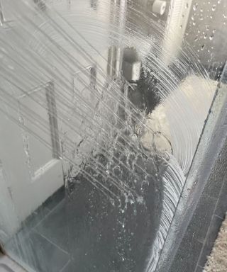 Rinsing a glass shower door with water from a shower head