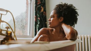 Woman sitting in the bath alone, looking out of the window thinking