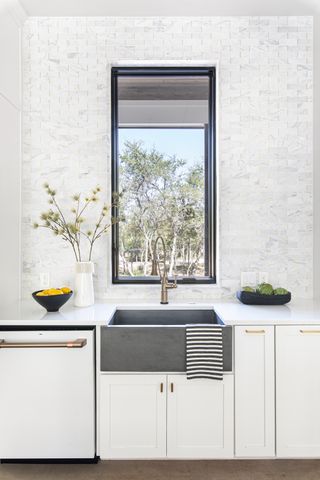 A white kitchen with a grey stone sink and a black framed window