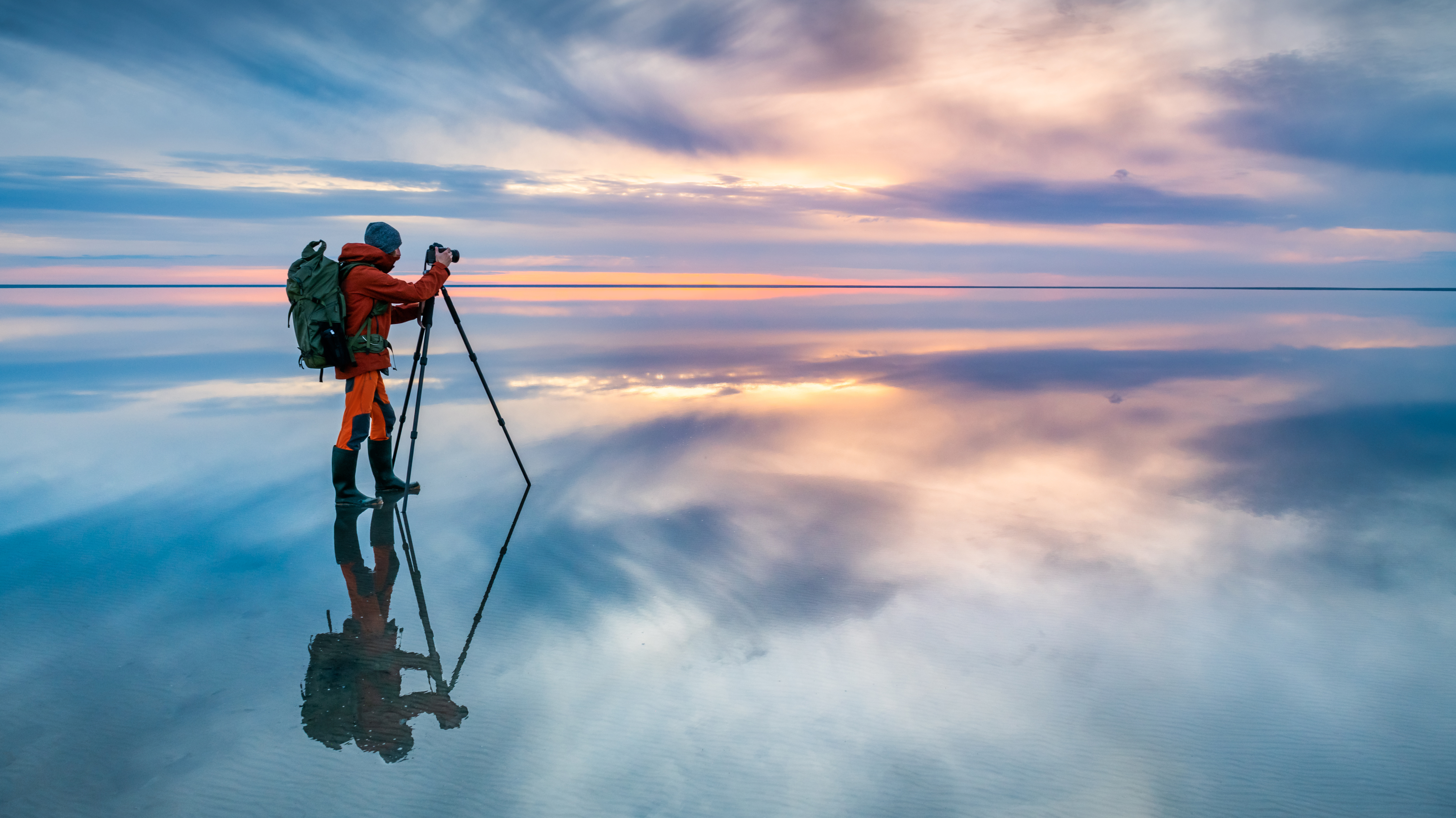 Photographer traveler taking photo of the salt lake at sunset. Blue sky with clouds are reflected in the mirror water surface. Professional photographer using tripod and dslr camera