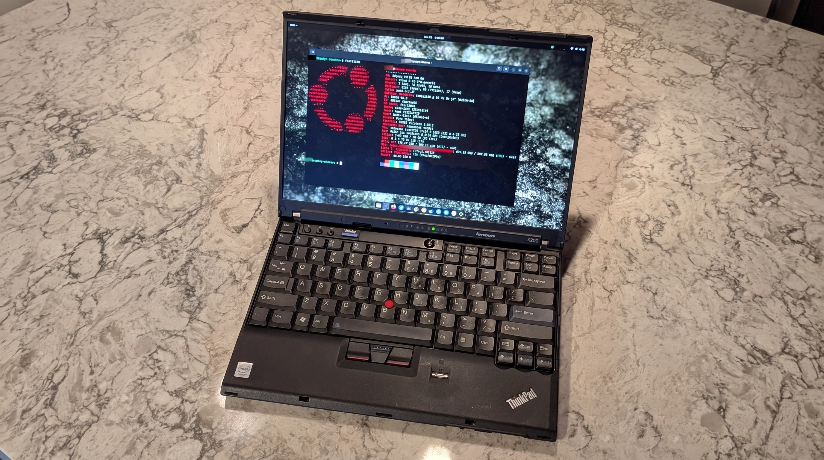 A Lenovo ThinkPad X200 laptop on a marbled surface, displaying code in various colors on its screen.
