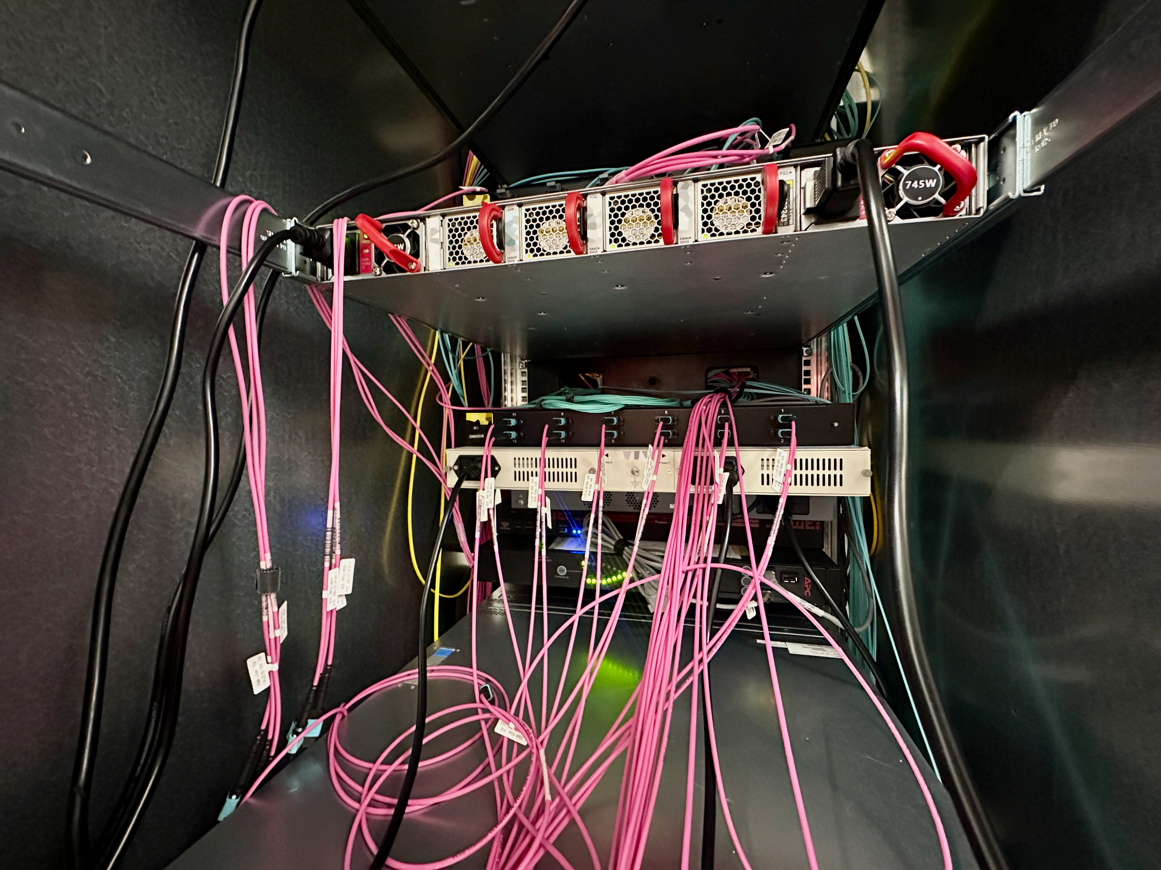 The rear of a server, with many neatly placed fiberoptic cables, with censored ID stickers