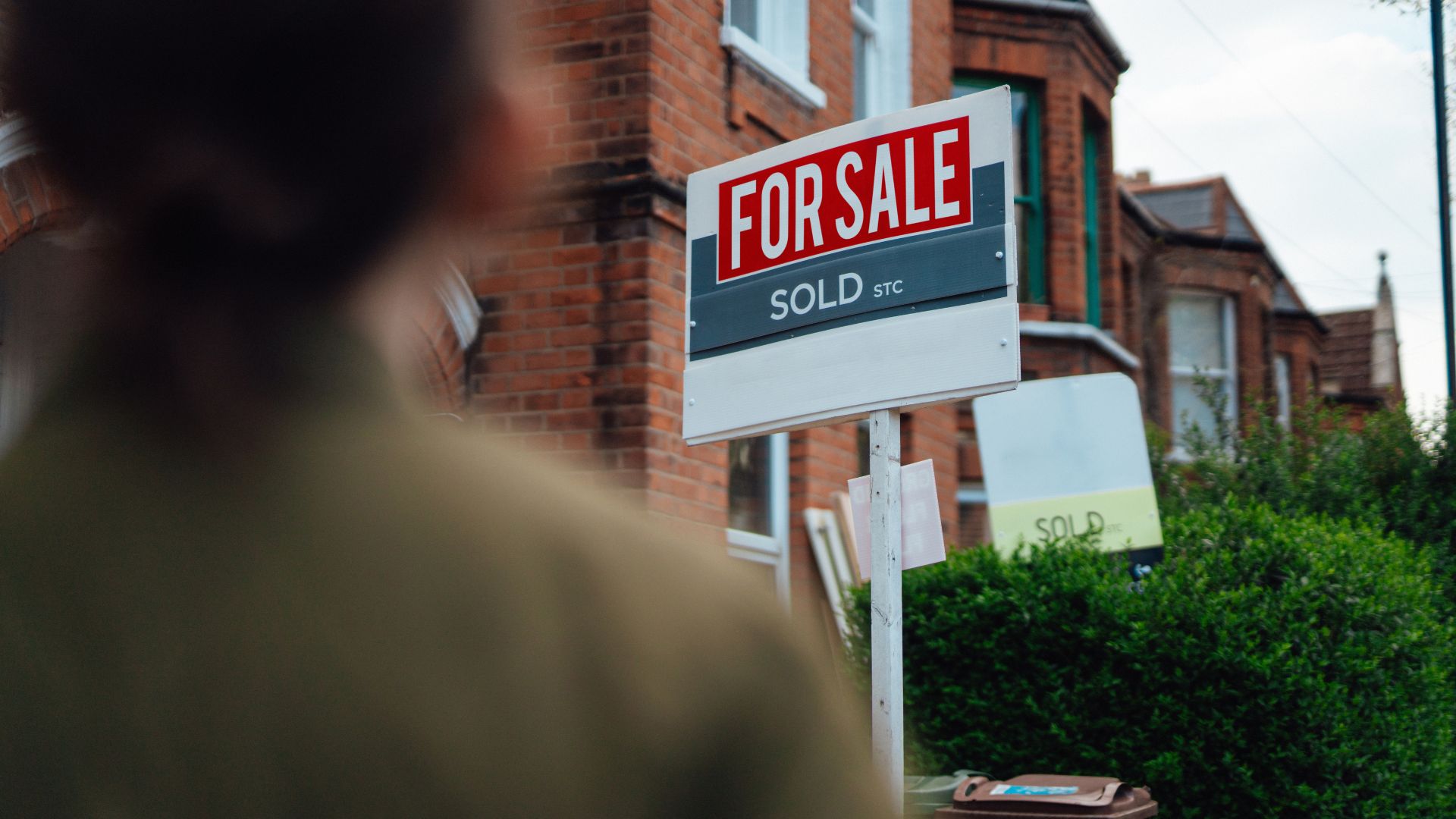 picture of woman stood looking at for sale sign on street