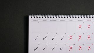 A photo of a calendar with four working days ticked, and the other days of the week crossed out, to represent a four-day week. The calendar is set against a dark grey surface.