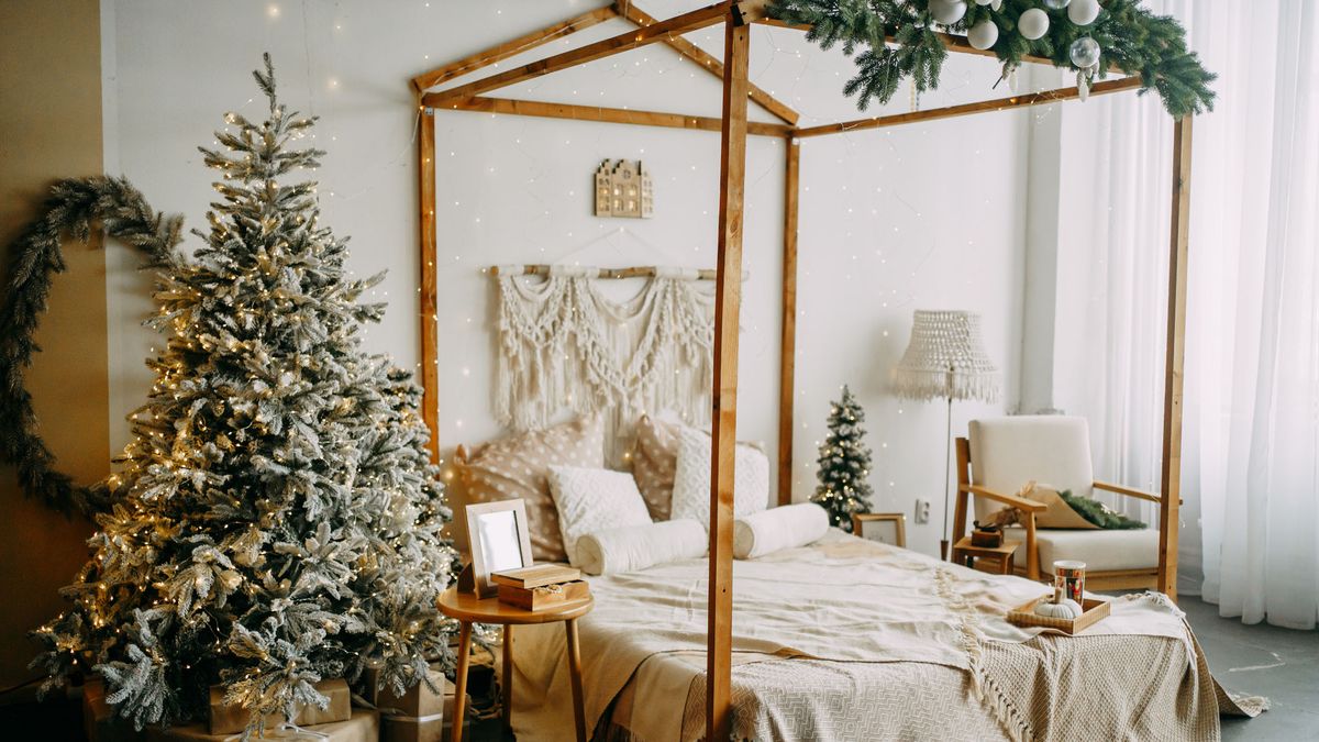 Image shows a green christmas tree with bright lights in a cozy bedroom decorated for the holidays