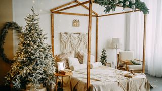 Image shows a green christmas tree with bright lights in a cozy bedroom decorated for the holidays