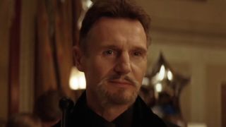 Liam Neeson smirks as he's introduced at a party in Batman Begins.