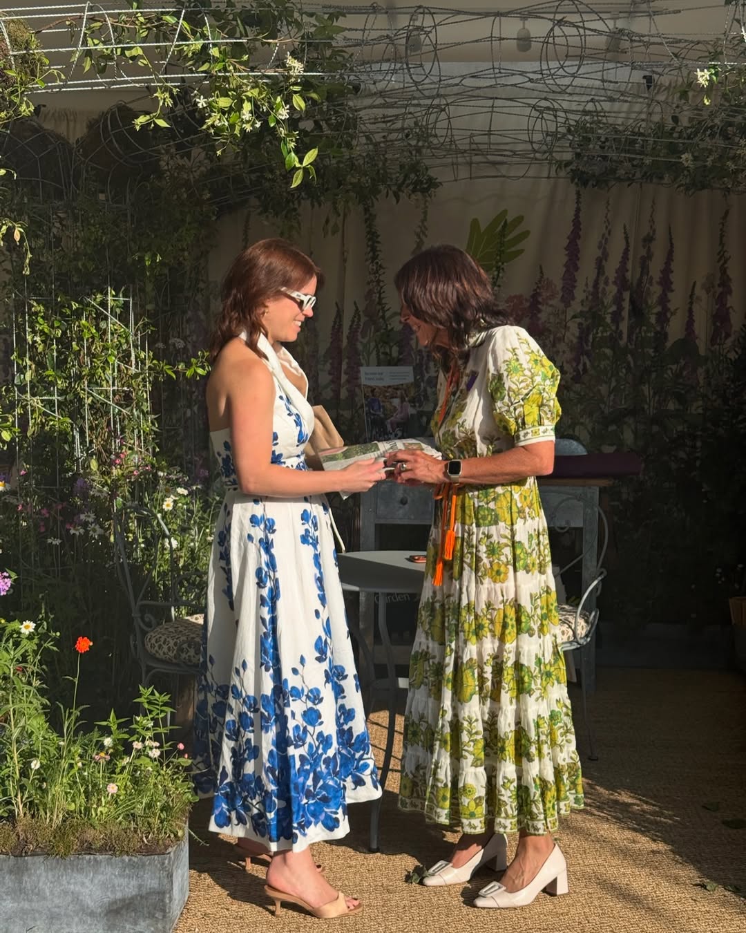 Princess Eugenie talking to a woman at the Chelsea Flower Show in a white dress with blue flowers