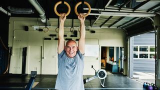 Man stretching out shoulders by hanging on gymastic rings in gym