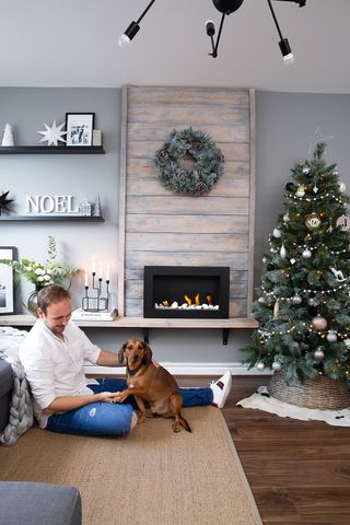 JT plays with dog Rocco in the grey living room with wood panelled fireplace and white and grey decorated Christmas tree