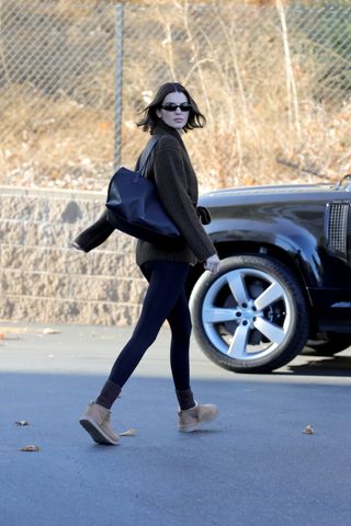 A photo of Kendall Jenner pairing a brownish-green wrap cardigan from The Row with light brown Ugg boots.