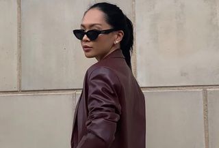 Woman wearing oxblood red suit, standing in front of wall taking outfit picture.