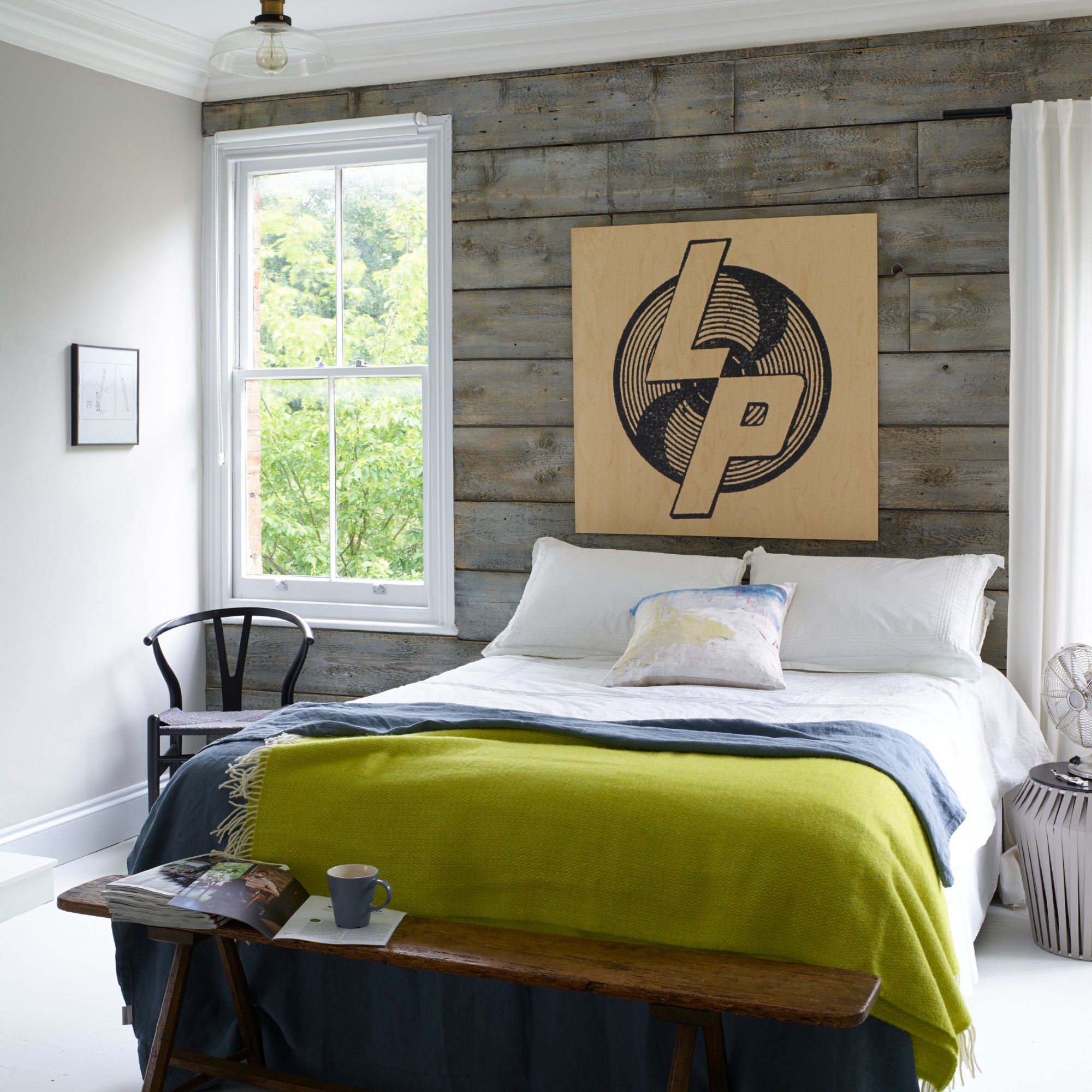A bedroom with a panelled feature wall, a wooden bench at the foot of the bed and a chartreuse green throw on the bed