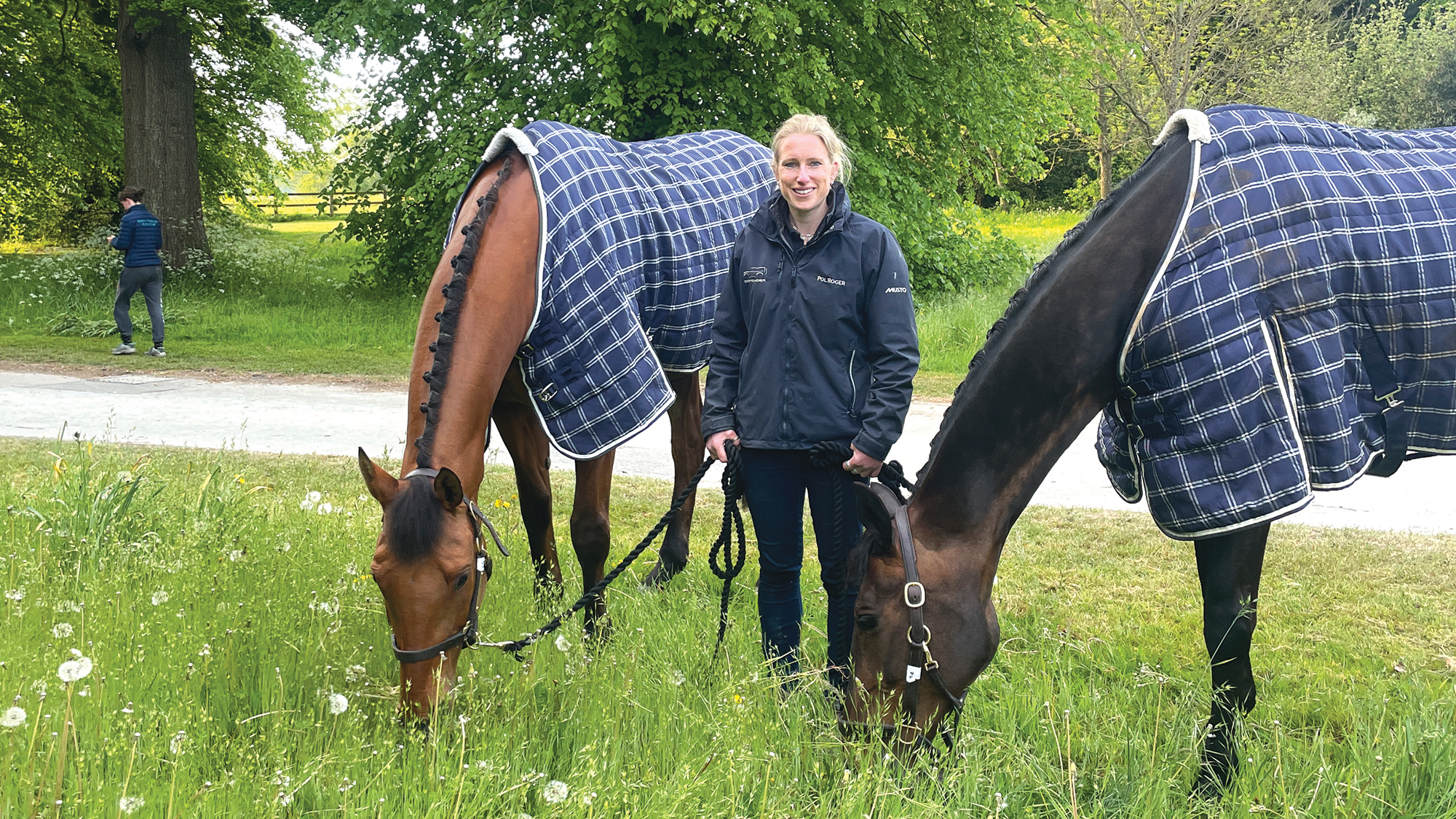 Groom Jess Errington hand grasses two of Harry Meade's event horses, which are both plaited up and wearing blue checked rugs