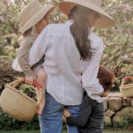 Meghan Markle wears a white shirt and blue jeans while she carries daughter Princess Lilibet and hugs son Prince Archie