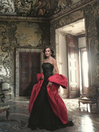 Queen Letizia wearing a black strapless evening gown and red stole posing in the Spanish royal palace