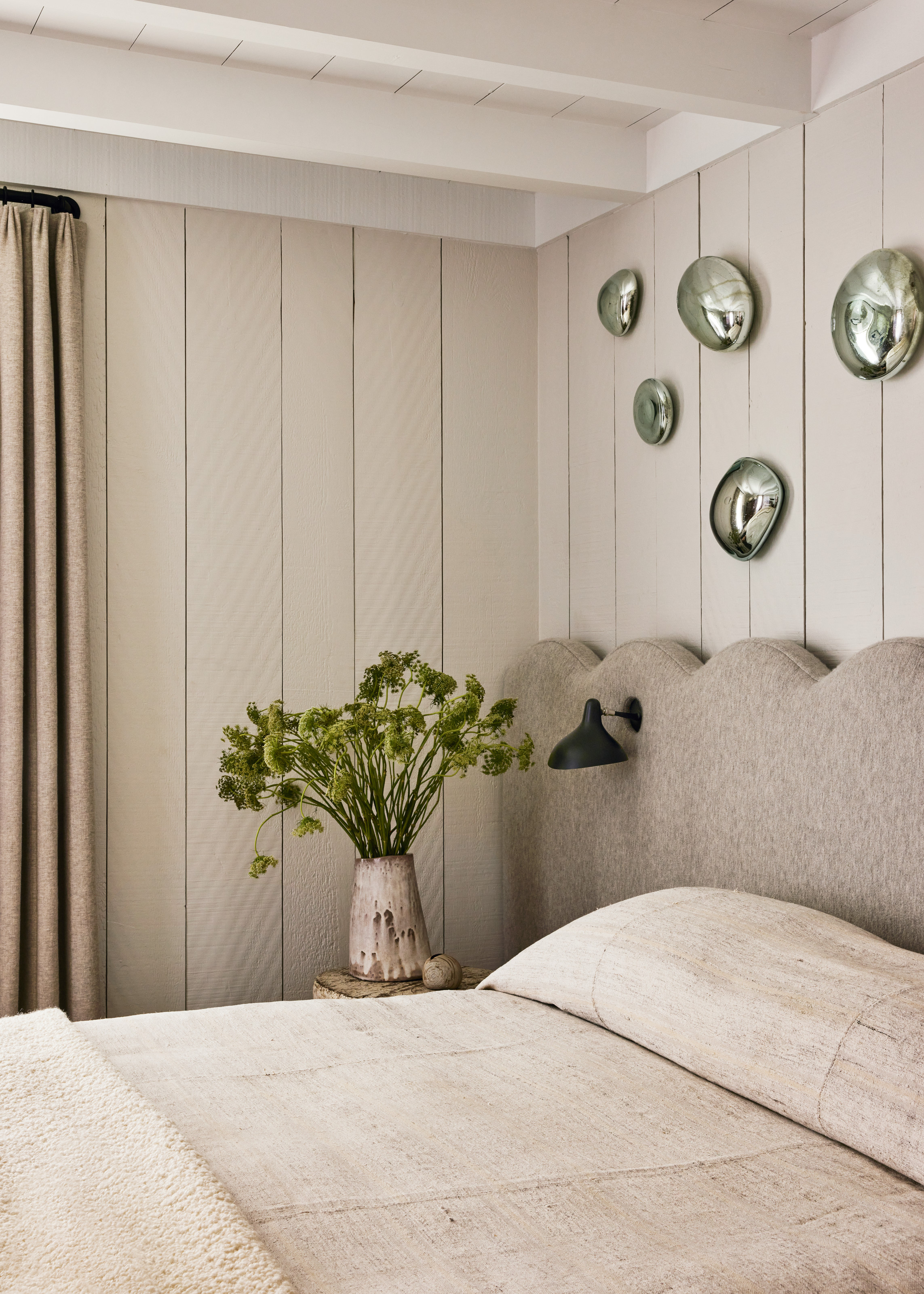 White panelled bedroom with wavy grey upholstered headboard and cream bed linen