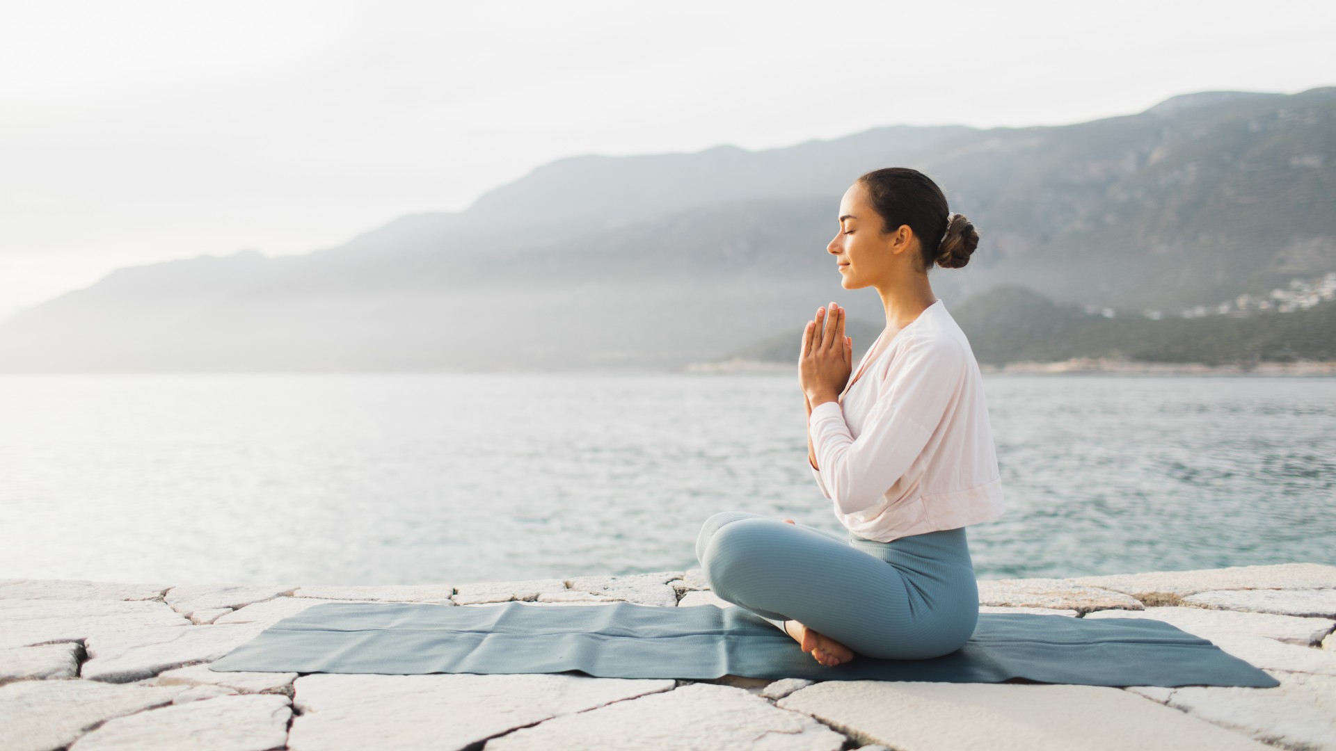 Woman meditating by the ocean on a mat