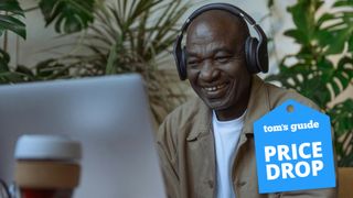 Man smiling at laptop wearing headphones and Tom's Guide logo