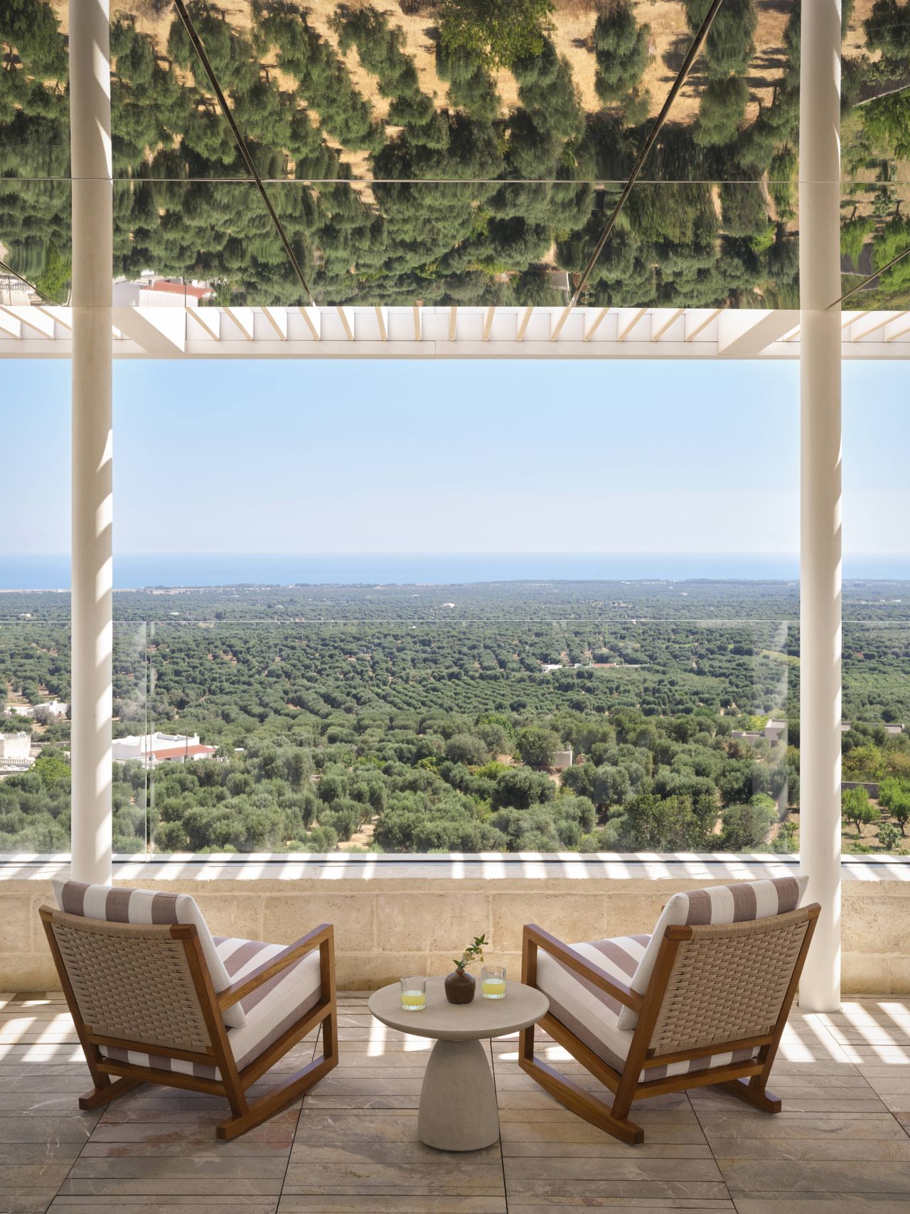 A design hotel's terrace boasts stripy loungers with creamy textiles, sandy marble surfaces, an infinity pool, and endless views over the surrounding landscape.