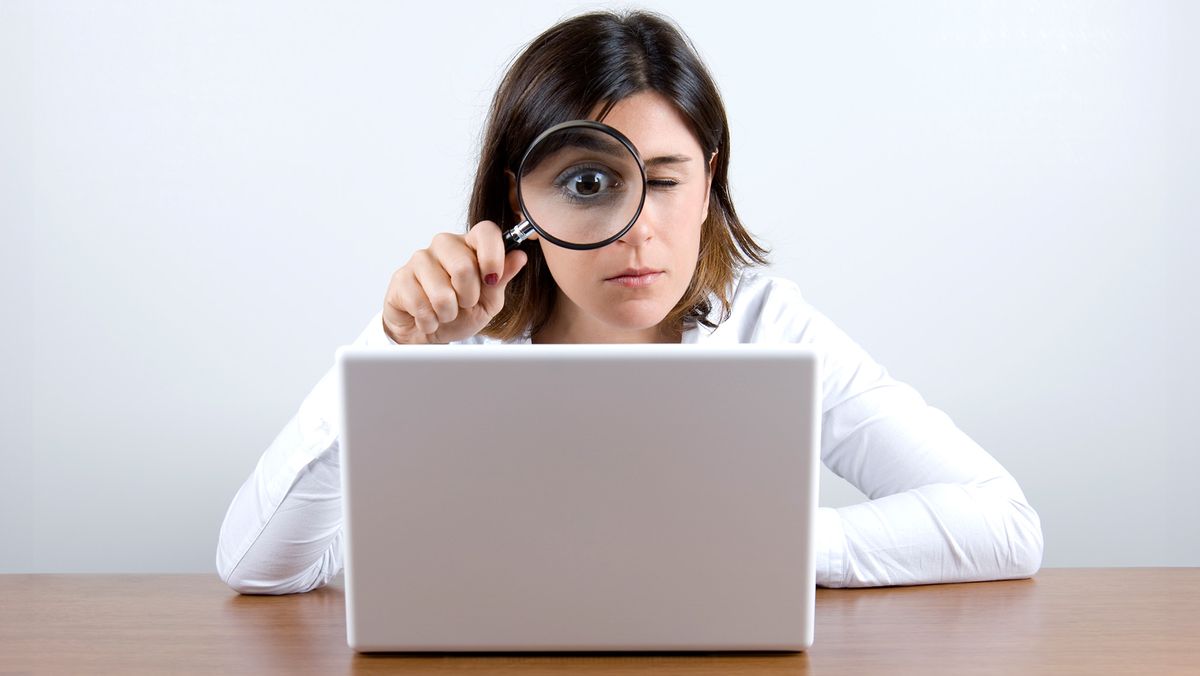 Woman looking at a laptop screen through a magnifying glass held up to her face