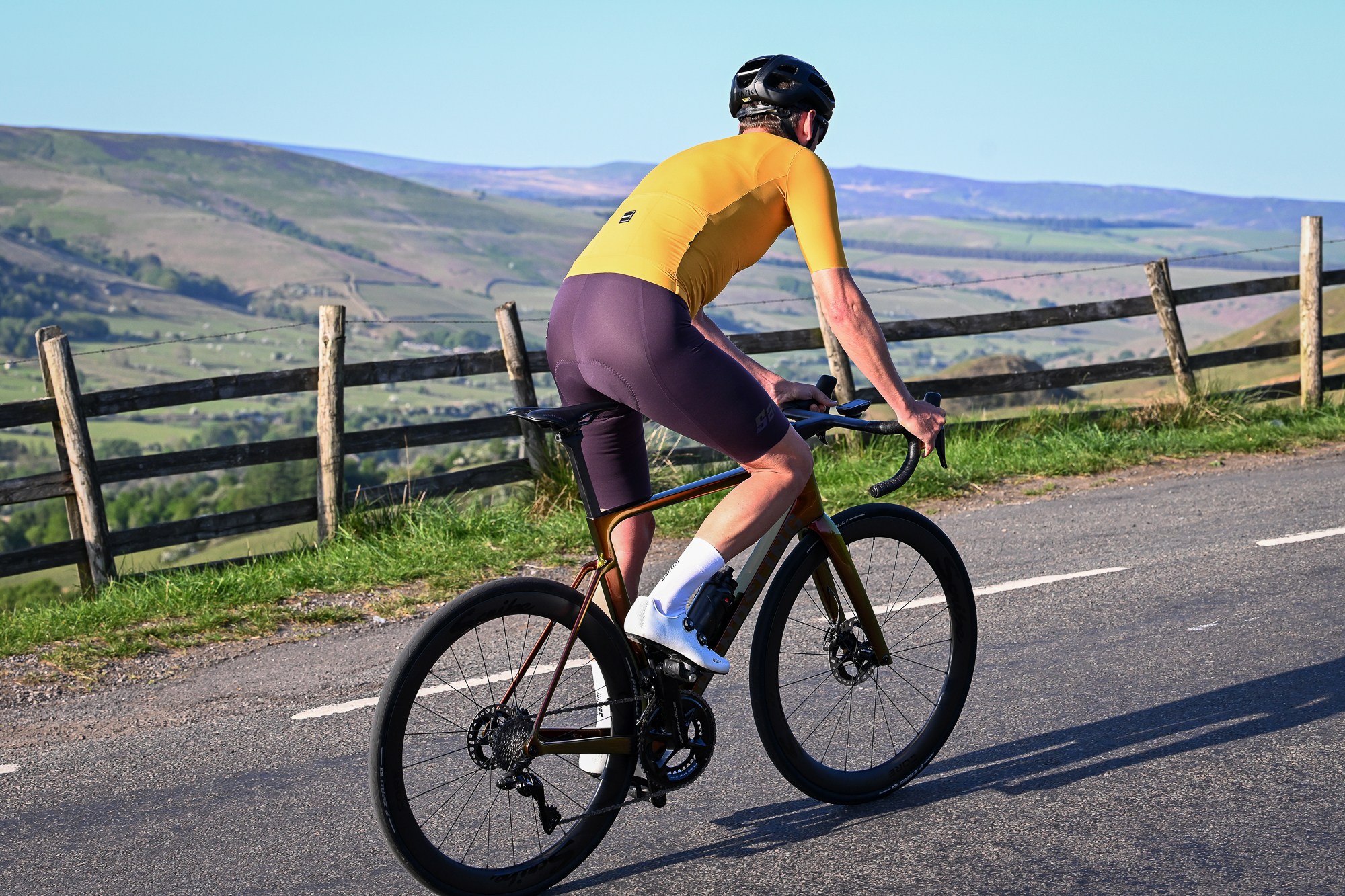 man riding a bike out of the saddle wearing purple shorts and a yellow jersey