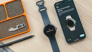 Google Pixel Watch 3 on a desk next to Pixel 9 smartphone showing a screen prompting users to sign in to their Google account