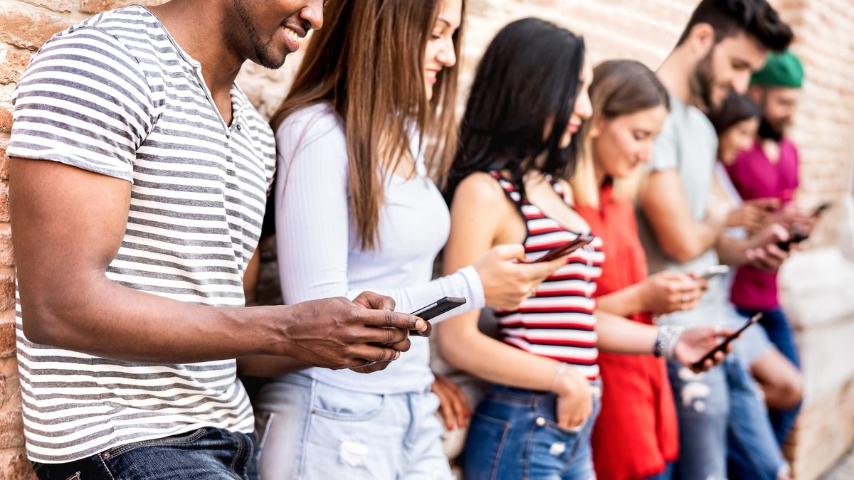 Group of friends using smartphones while leaning along a brick wall.