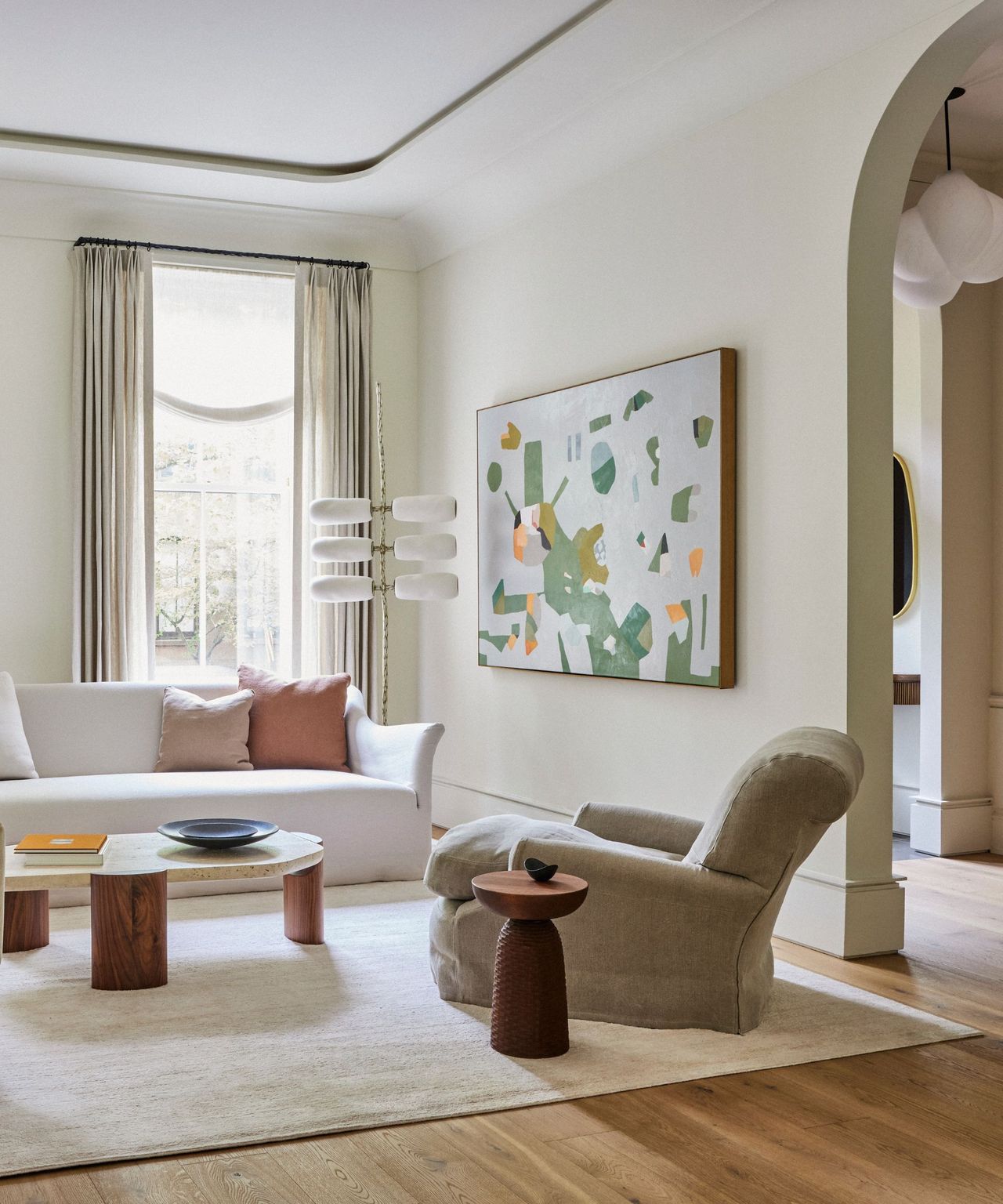 A brownstone living room with an arched doorway, white sofa, and lush area rug