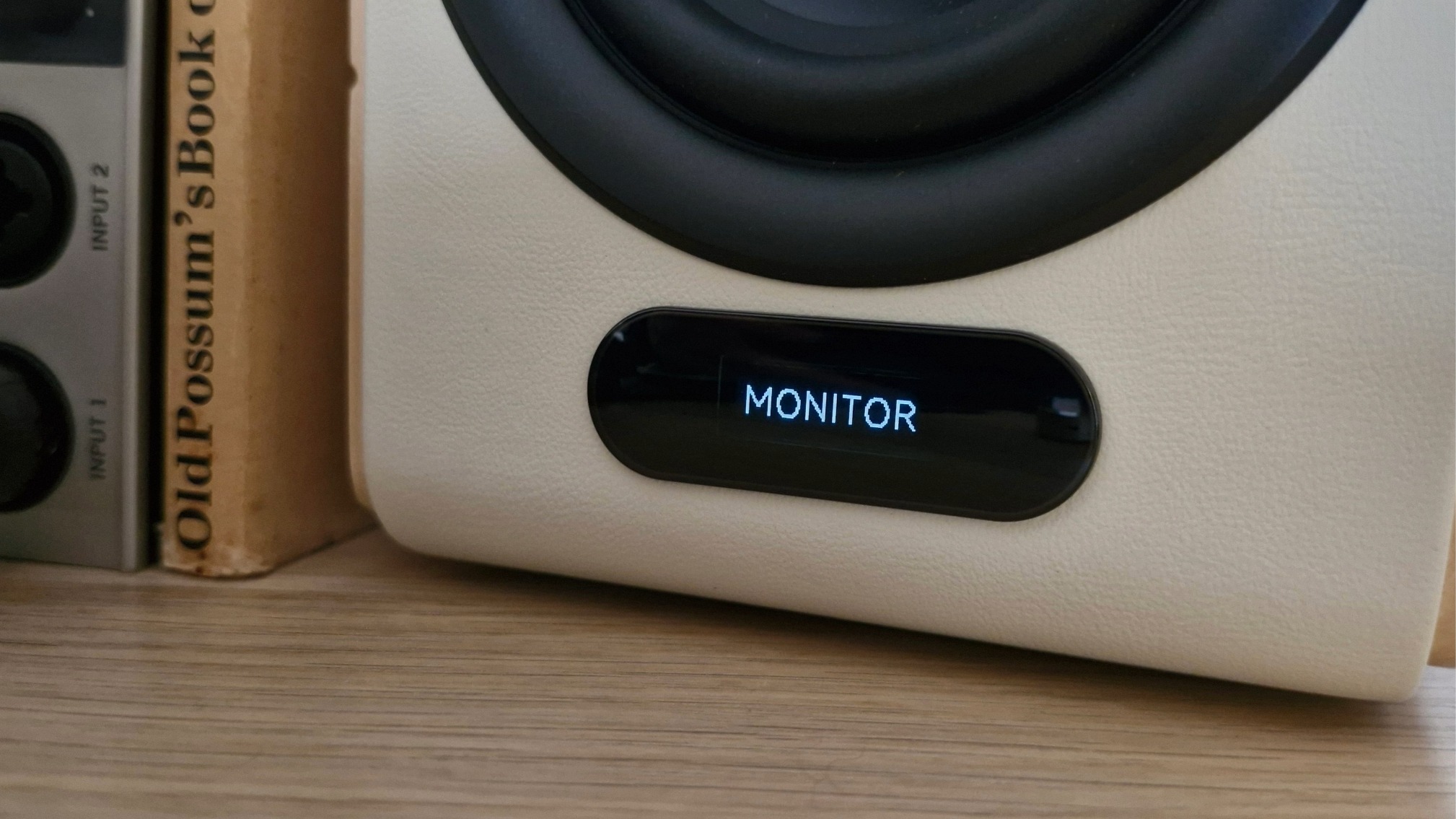 Closeup of the OLED panel of the Edifier S880DB MKII active bookshelf speakers, displaying the selected EQ mode 'Monitor', on a wooden surface