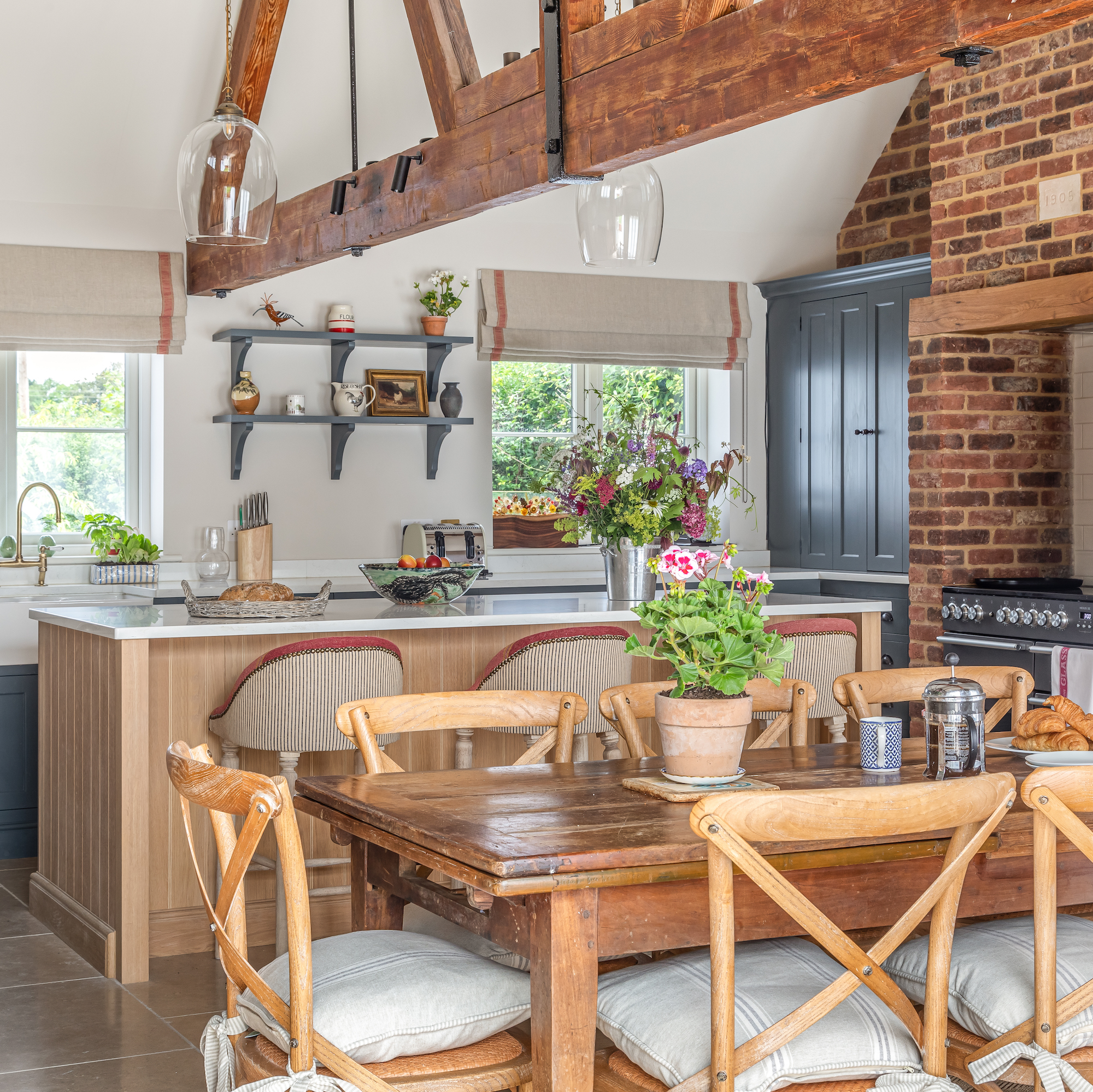 kitchen and dining area in barn conversion with wooden beams on ceiling and wooden island unit and blue cabinetry next to wooden farmhouse dining table with chairs