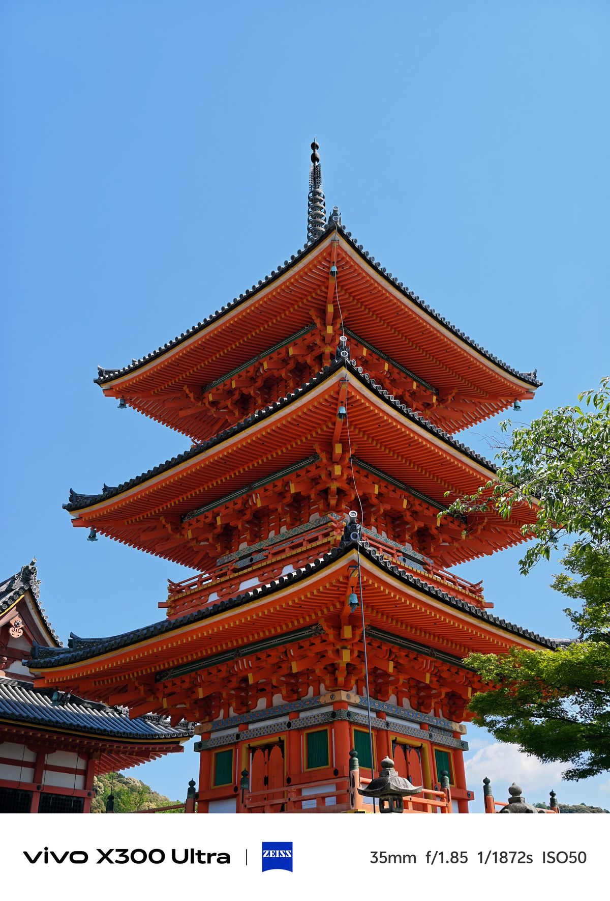 A low-angle shot of a tall, vibrant orange three-story traditional pagoda under a clear blue sky.