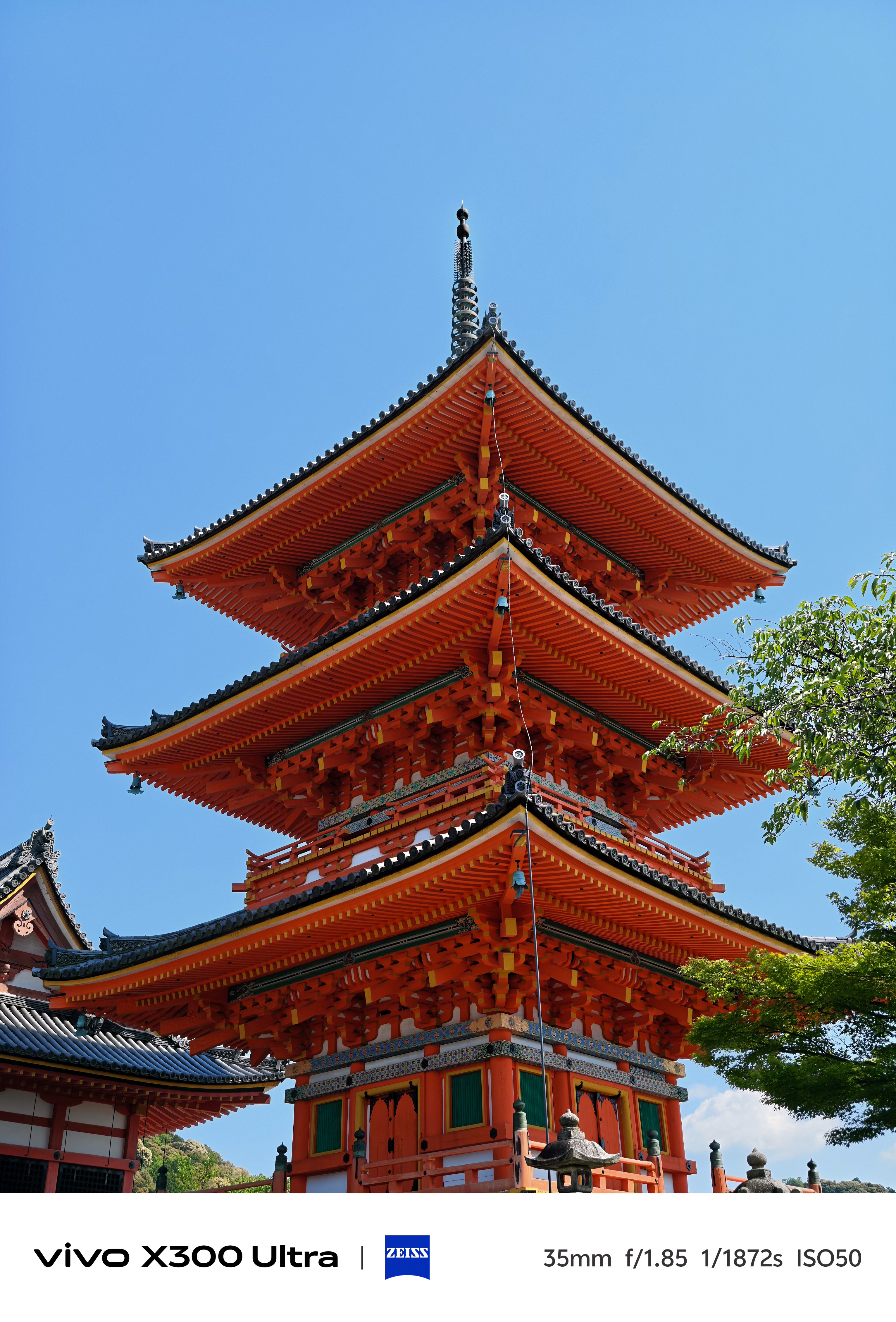 A low-angle shot of a tall, vibrant orange three-story traditional pagoda under a clear blue sky.
