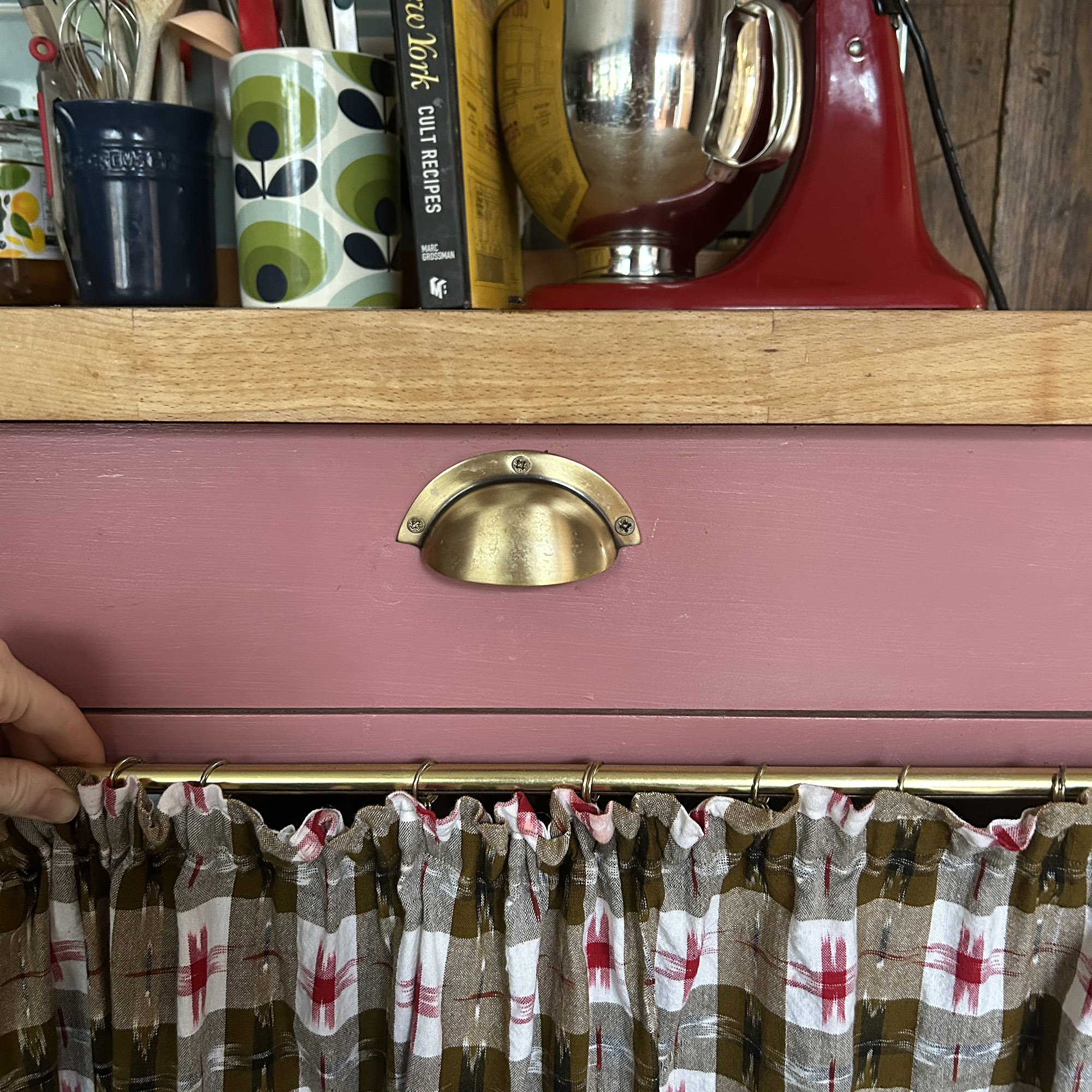 pink kitchen cabinet with patterned curtain across the front and red kitchenaid on top