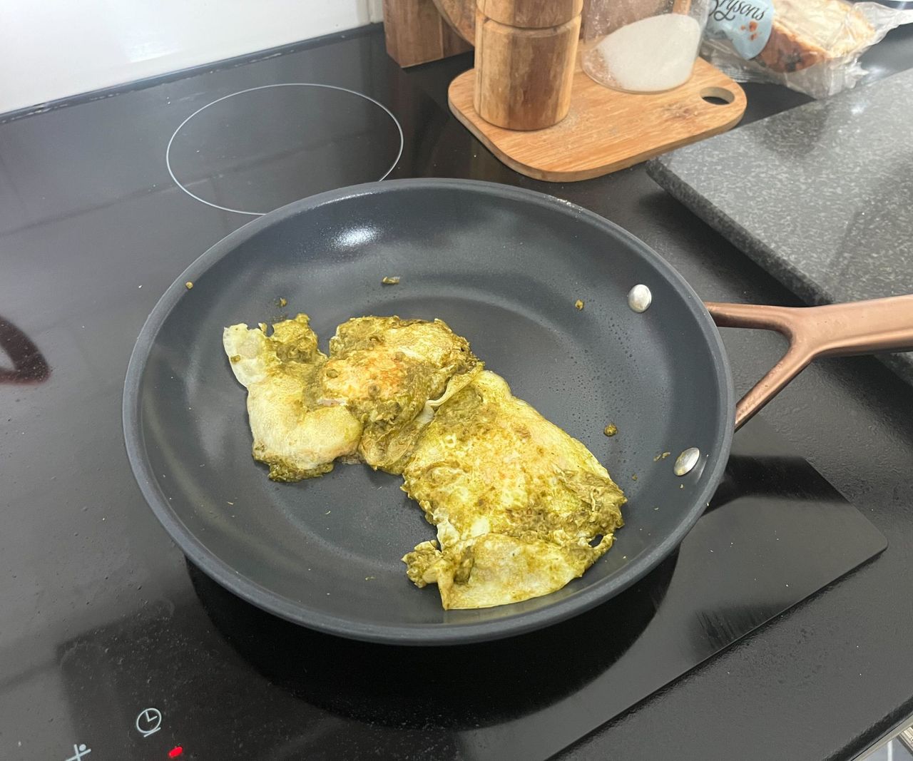 Fried eggs and green pesto in a small blue ceramic frying pan.