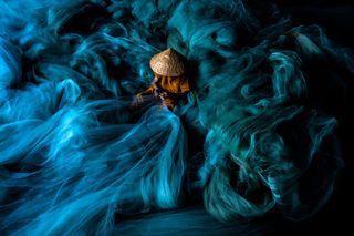 an individual sitting in the middle of a large blue net resembling waves