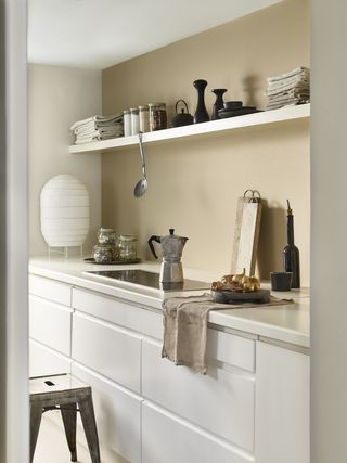 A kitchen with white cabinets and countertop and a beige, light brown feature wall