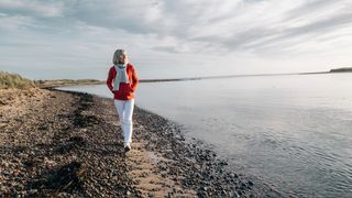 A woman wearing a red coat and white trousers walking along shoreline to help her sleep