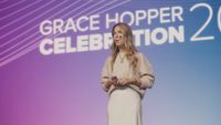 A speaker presents on stage in front of a Grace Hopper Celebration backdrop at a past event