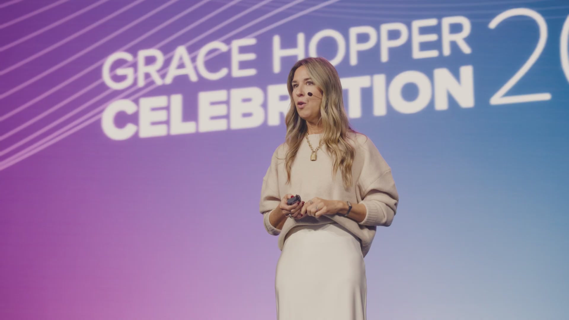 A speaker presents on stage in front of a Grace Hopper Celebration backdrop at a past event