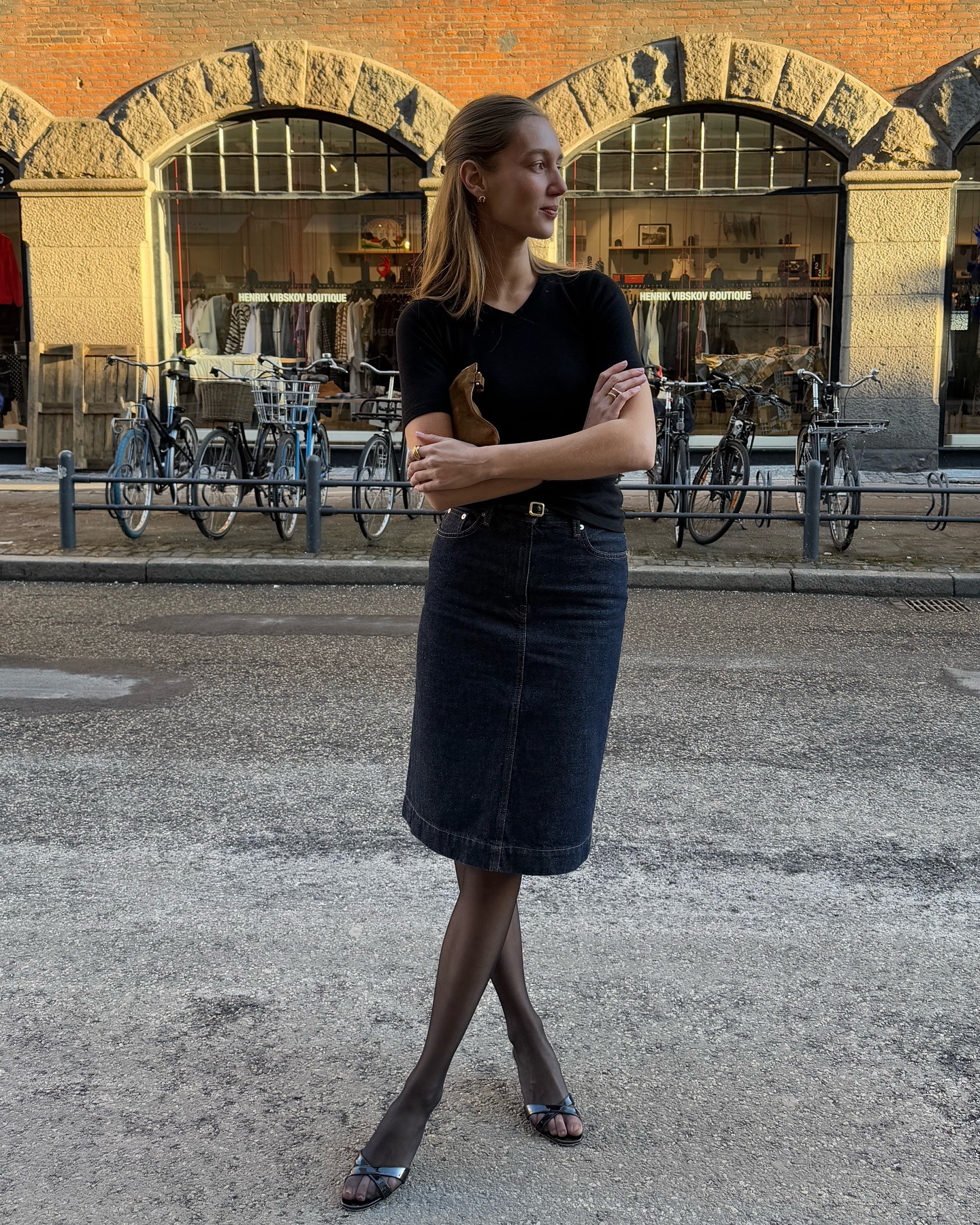 Amalie Moosgaard wearing a black tee, denim pencil skirt, tights, and sandals.