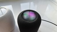 A black Apple HomePod 2 on a white surface with its top panel visible.