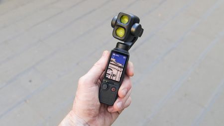 DJI Osmo Pocket 4P vlogging camera in a person's hand in a city street, screen vertical