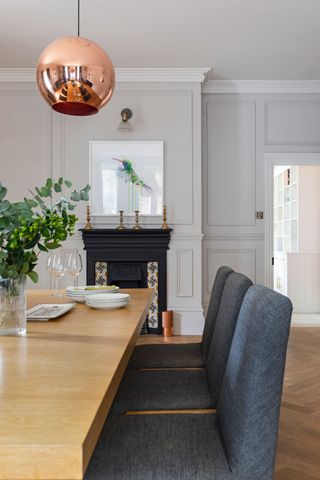 dining room with pale wood table and gray chairs with copper pendant light and period fireplace beyond and cream walls
