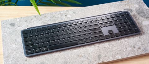 a black and grey budget wireless Bluetooth keyboard with a full-size layout and a numerical keypad is photographed against a blue background