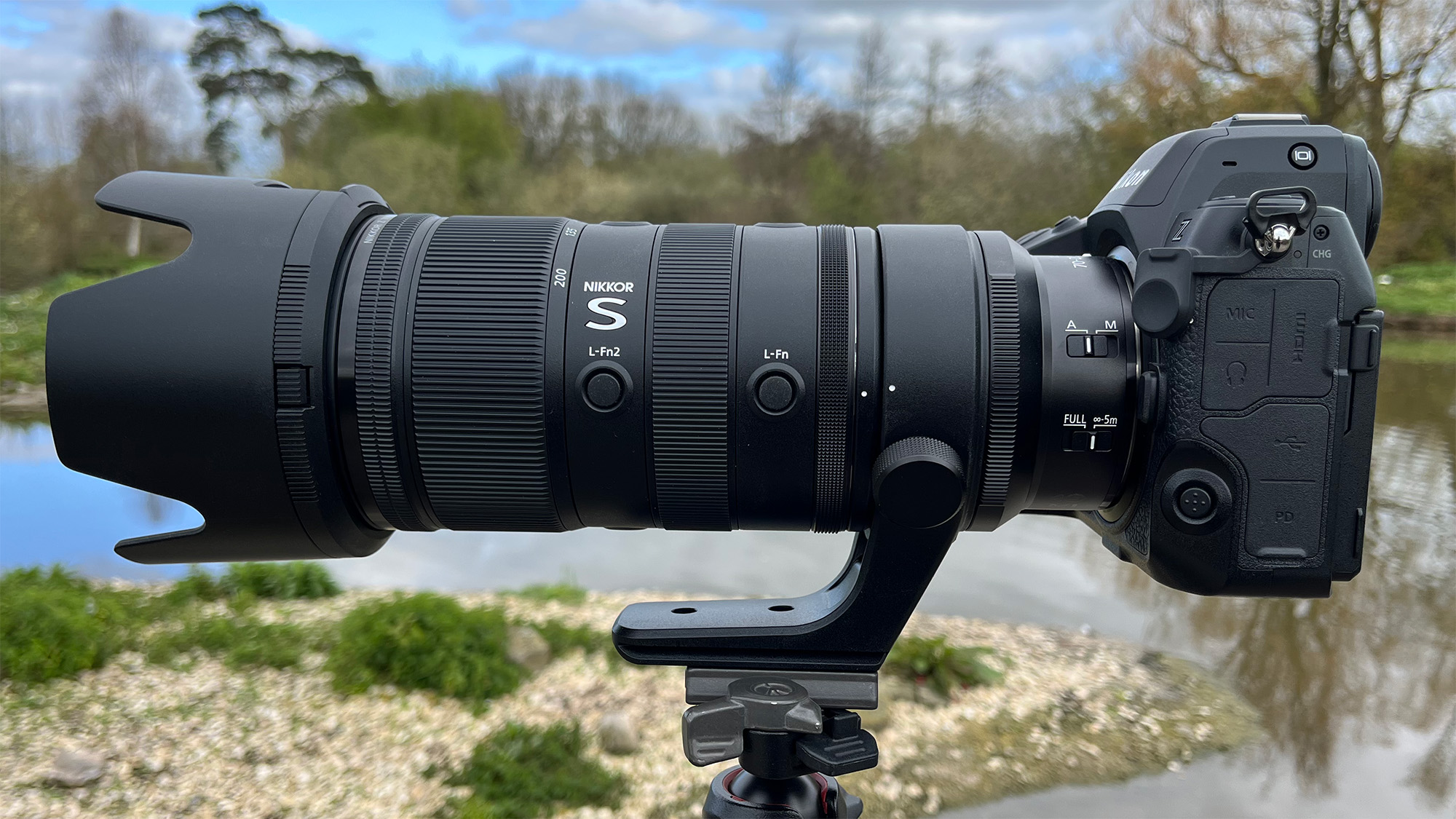 Mike Harris holding Nikon Z 70-200mm f/2.8 VR S II by a lake with vegetation and trees in the background
