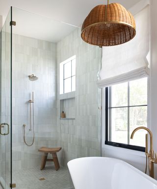 A white tiled bathroom with a shower, standing tub, and rattan light fixture