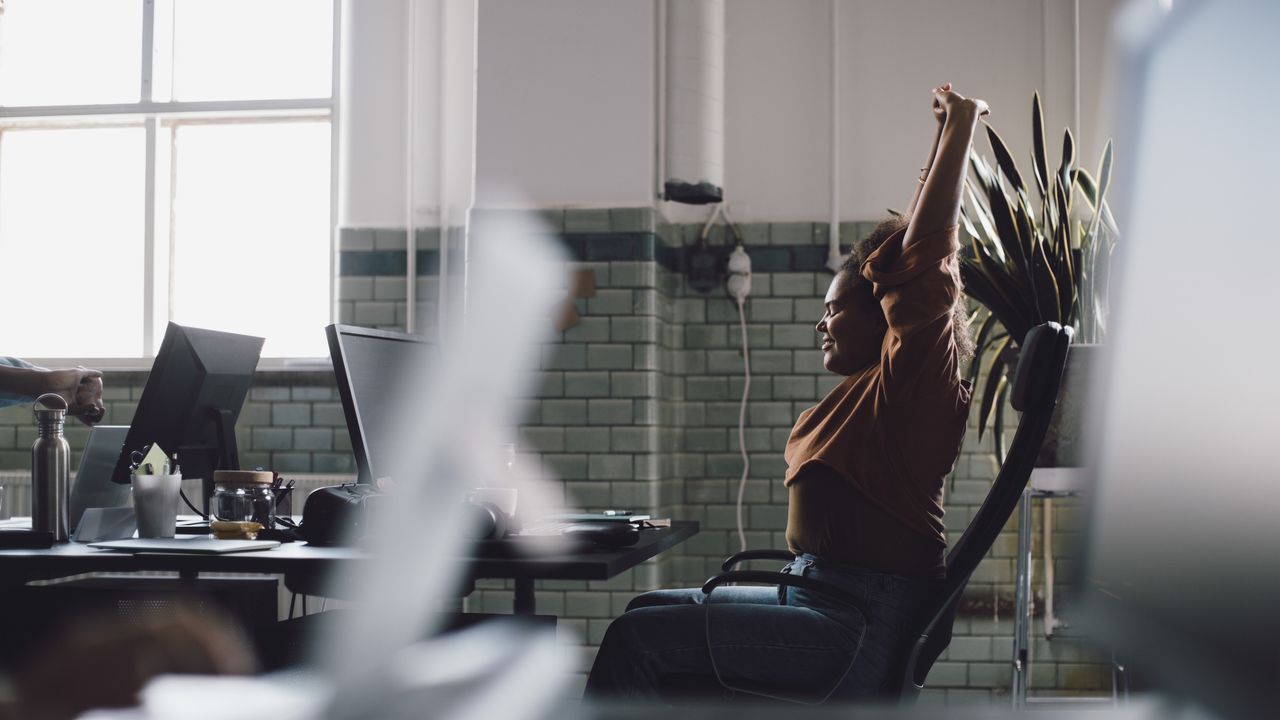 Woman sitting at office desk stretches her arms above her head